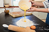 Teenage girl pouring egg yolks into flour on kitchen counter