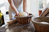 Woman placing dough into proofing basket in kitchen