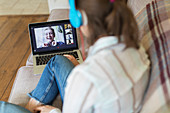 Teenage girl with laptop video chatting with friends on sofa