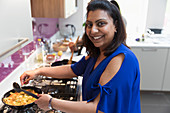 Portrait happy Indian woman cooking food at stove in kitchen