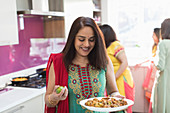 Indian woman in sari with plate of food in kitchen