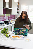 Woman with credit card shopping online at laptop in kitchen