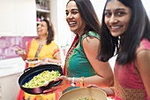 Happy Indian women in saris cooking food in kitchen