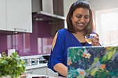 Smiling woman drinking tea at laptop in kitchen