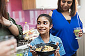 Happy Indian girl with bowl of food in kitchen