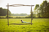 Branch frame over young woman laying in sunny grass field