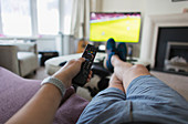 POV man with remote control watching soccer match on sofa