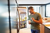 Man eating yogurt at open refrigerator in kitchen
