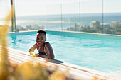 Happy young woman in sunny, luxury swimming pool