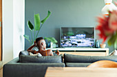 Young woman watching TV on living room sofa