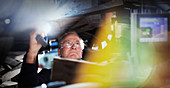Focused male mechanic with flashlight under car