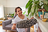 Mature woman with duster dusting living room