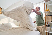 Man with duvet making bed in bedroom