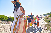 Family carrying folding chair and toys on beach