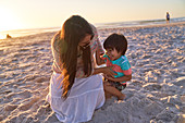 Playful mother tickling son on sunset beach