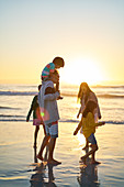 Family wading in ocean surf on beach at sunset
