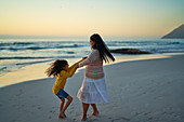 Mother and daughter spinning on ocean beach