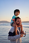 Father carrying son on shoulders on beach