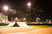 Young man skateboarding at skate park at night