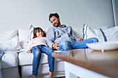Father and daughter relaxing on living room sofa