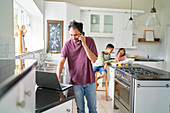 Man working at laptop in kitchen with kids eating