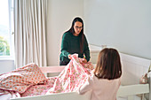 Mother helping daughter make bed