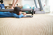 Girl using laptop next to father on treadmill