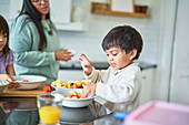 Cute boy eating fresh fruit in kitchen