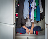 Boy hiding behind clothes in closet