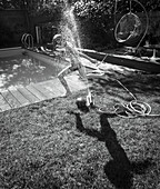 Boy running through sprinkler in summer backyard