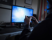 Boy playing videogame at computer in dark bedroom