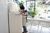 Woman in apron standing at open refrigerator