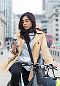 Woman on bicycle using smart phone in city