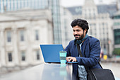 Businessman using laptop on city bridge railing