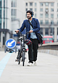Businessman walking bicycle on city bridge