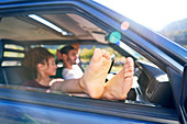 Young woman relaxing with bare feet out car window