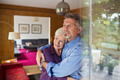 Happy senior couple hugging at living room window