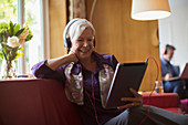 Senior woman using headphones and tablet on sofa