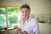 Senior man with smart phone and tea in kitchen
