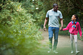 Father and daughter holding hands on path in woods