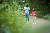 Father and daughter holding hands on path in woods