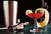 Roter Cocktail mit Zitronenschale und Oliven auf Bartheke