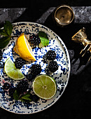 A blue and white plate with lemons, limes, blackerries, blueberries and mint