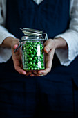 Person in apron standing with glass can of fresh green peas