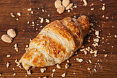 Croissant with golden crust on wooden table with crumbs of almond nuts