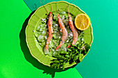 Garnelen auf grünem Teller mit halber Zitrone und Petersilie auf mehrfarbigem Hintergrund
