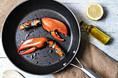 Lobster claws in pan, bottle of olive oil and half of juicy lemon