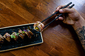 Sushi-Röllchen mit Reis und Fisch, garniert mit frischen Kräutern, auf Essstäbchen