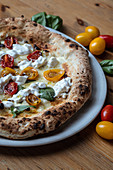 Crusty cheese pizza with sliced yellow tomatoes and olives decorated with basil leaves in wooden table