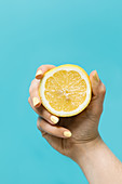 Anonymous female with yellow manicure showing half of ripe lemon on light blue background